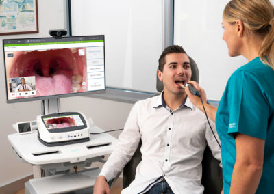 Dentist assistant performing live exam, pointing Visionflex GEIS in patient's mouth displayed on medical cart with video-conferenced doctor.