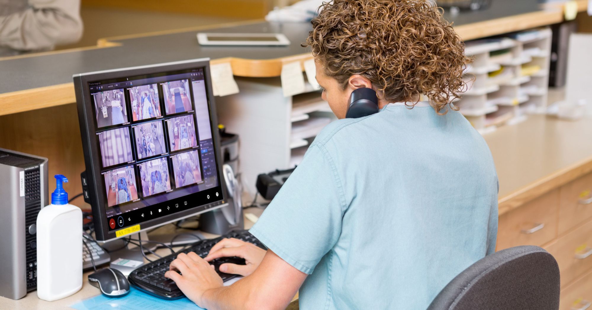 Nurse using telesitter solution to observe multiple patients from her desktop while speaking on the phone.